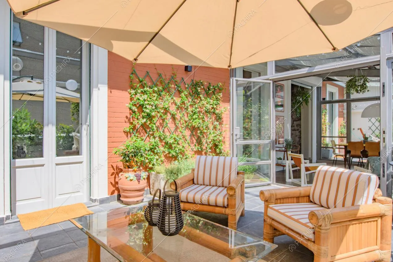 Poltrone e tavolino sulla terrazza con ombrellone, porta-finestra e veranda