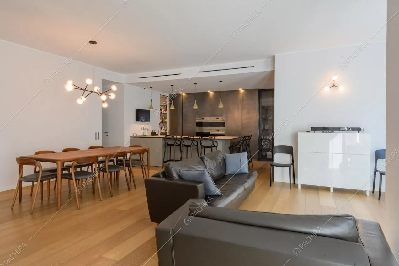 Divani in pelle nera nella zona living con tavolo da pranzo in legno e cucina con penisola