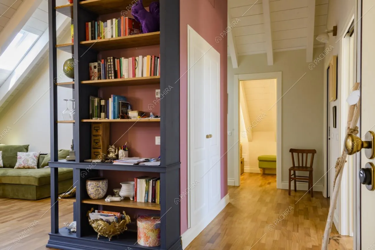 Pareti colorate, mobile libreria con mensole, travi a vista e parquet