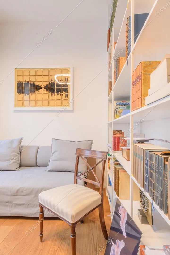 Studio con divanetto grigio, libreria, pavimento in parquet e pareti bianche