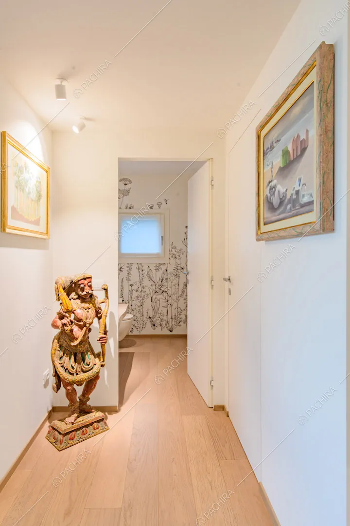 Lungo corridoio con pavimento in parquet e pareti bianche conduce al bagno