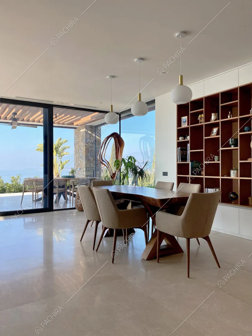 Nella zona living tavolo da pranzo in legno, pareti bianche e vetrate con vista sul mare