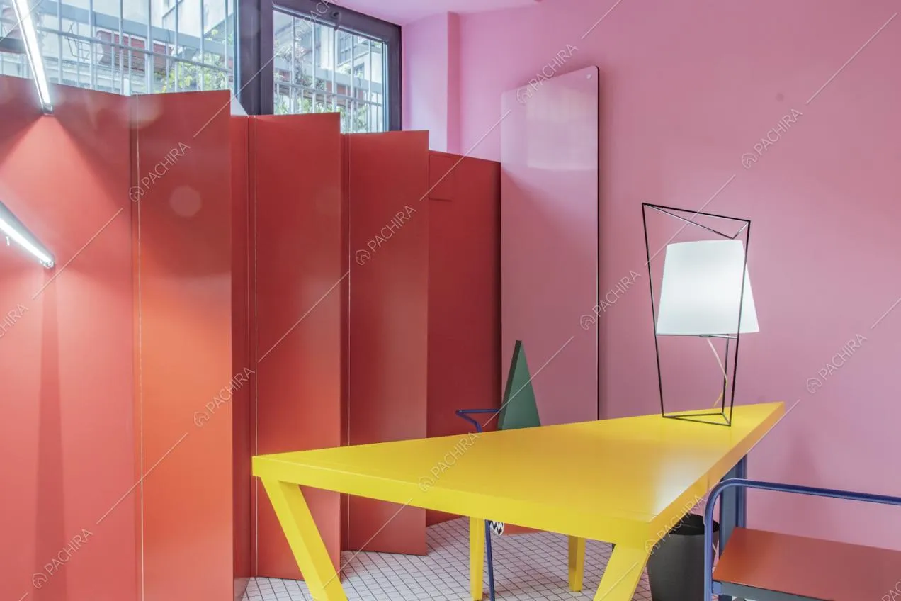 Un separè rosso e una lampada di design su un tavolo triangolare giallo