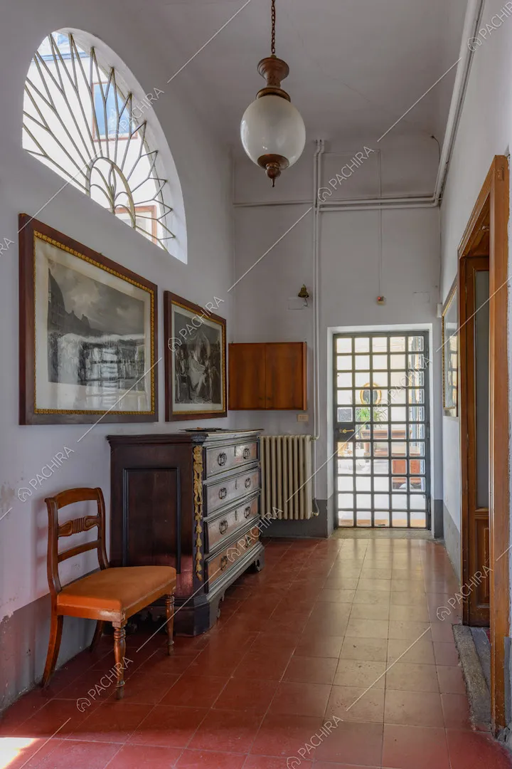 Pavimento in piastrelle rosse, pareti bianche e finestra a mezzo cerchio con decorazione in metallo