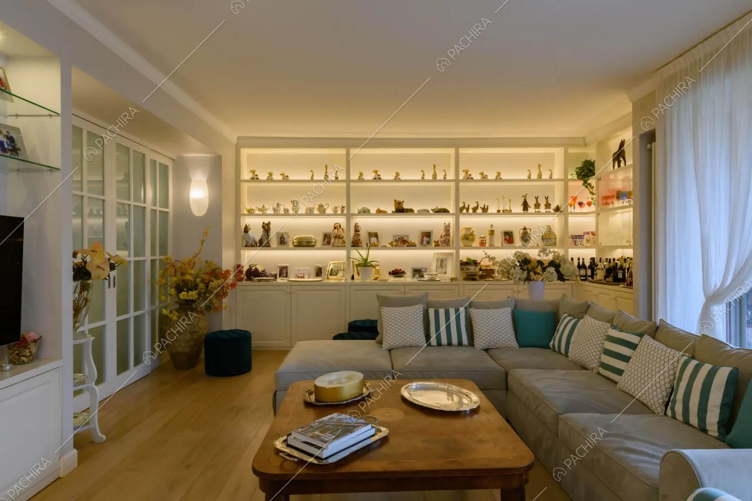 Salotto con divano grigio angolare, pavimento in parquet e porta in vetro con infissi bianchi
