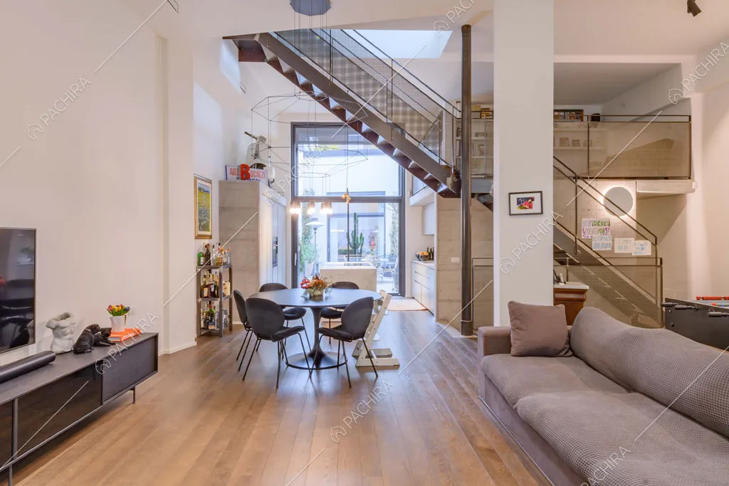 Divano grigio e tavolo da pranzo rotondo nella luminosa zona living con grande vetrata