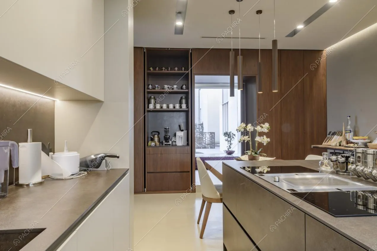 Cucina bianca con fornelli a induzione sull'isola e parete dall'effetto legno che porta negli altri ambienti