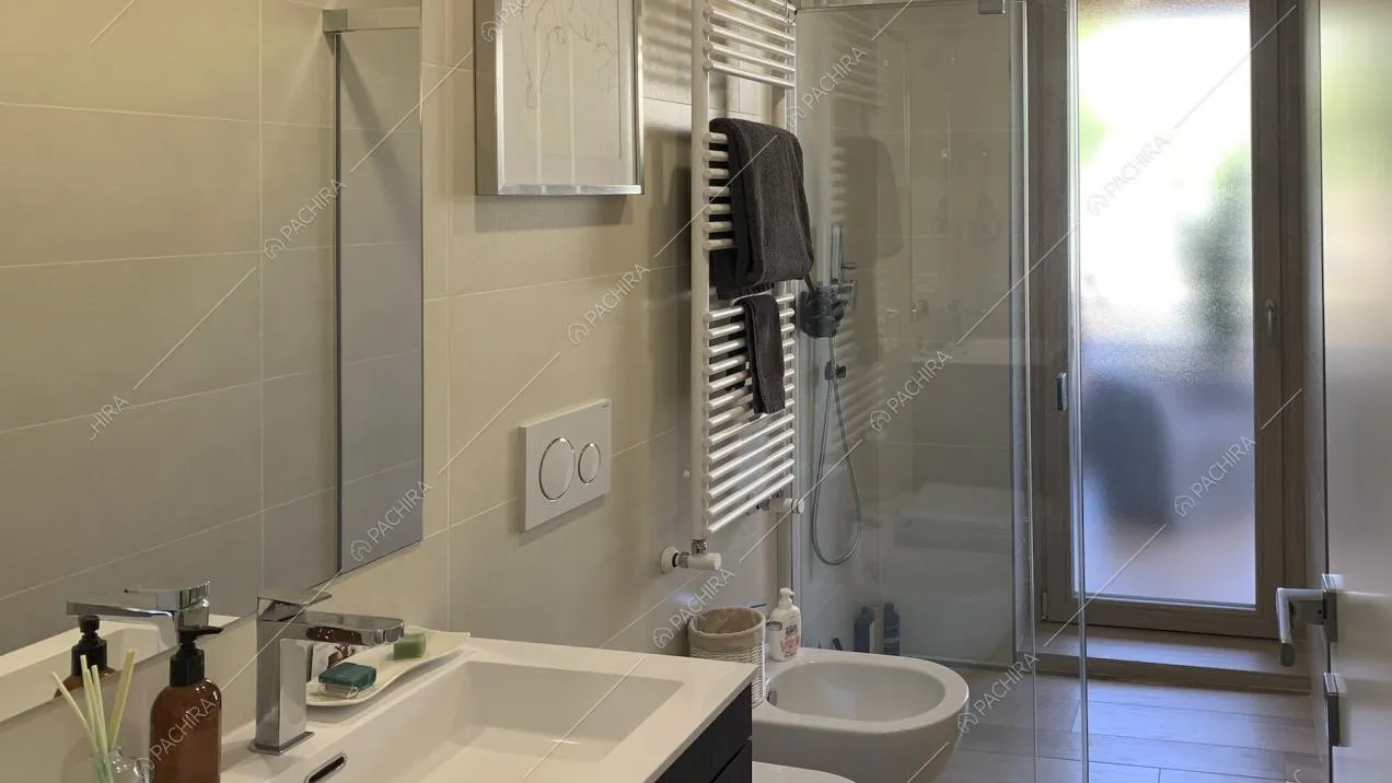 Bagno con piastrelle chiare, radiatore a parete e doccia