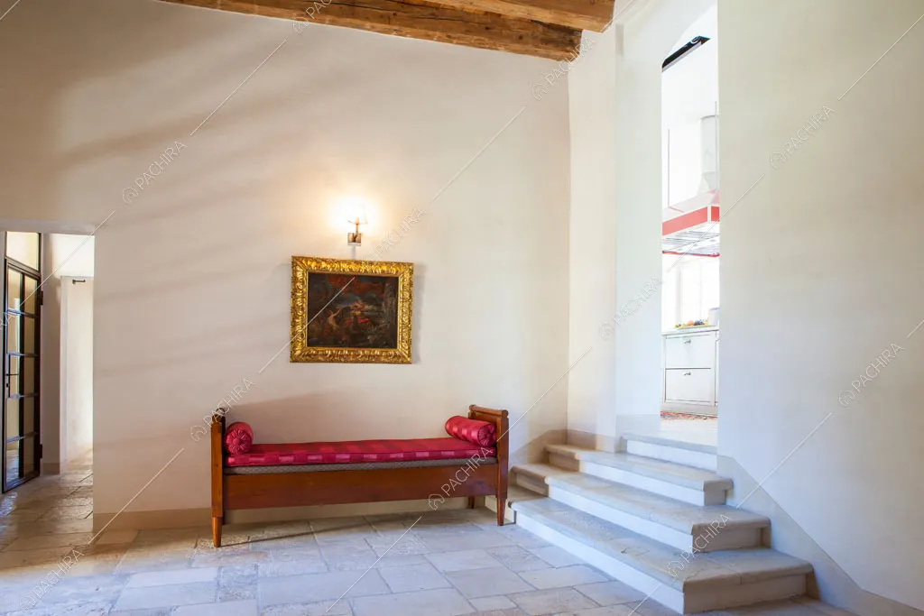Luminoso atrio con panca in legno, pareti bianche e scorcio sull'isola della cucina