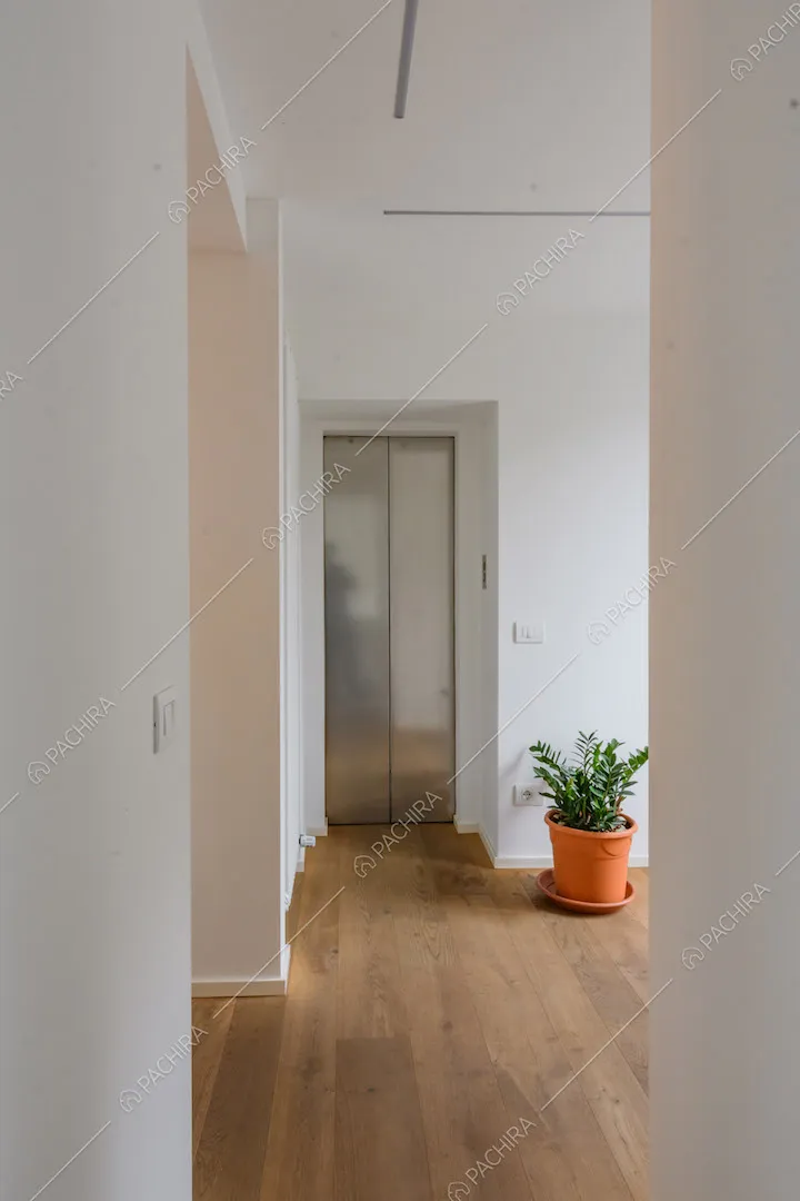 Corridoio con pavimento in parquet, pareti bianche e ascensore