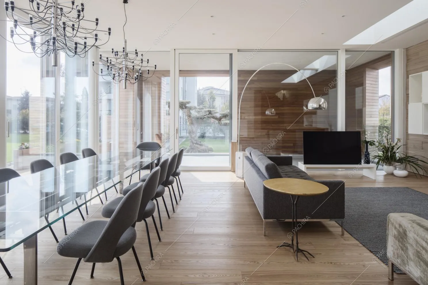 Ampia sala con lungo tavolo da pranzo, lampadari di design, pareti in vetro che portano alla veranda e divani