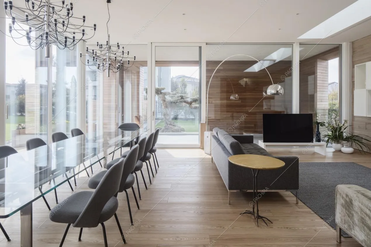 Ampia sala con lungo tavolo da pranzo, lampadari di design, pareti in vetro che portano alla veranda e divani