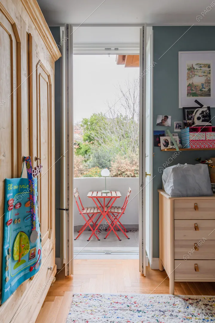 Camera da letto con pareti azzurre e porta-finestra che conduce al balcone con tavolo da esterni