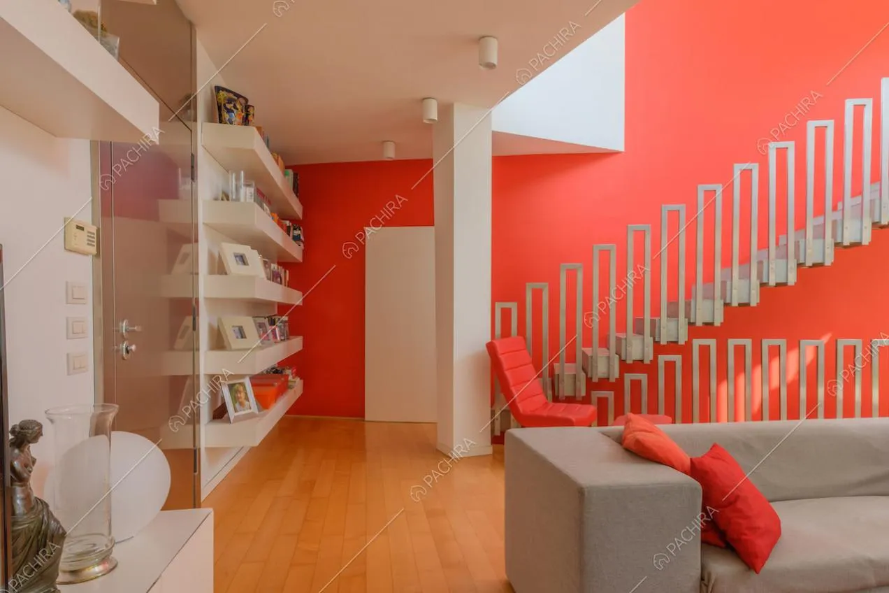 Pavimento in parquet nella zona living con scale, parete rossa e divano grigio