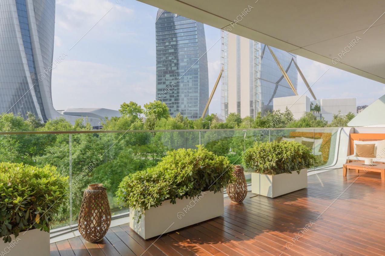 Parapetto in vetro sulla terrazza con pavimentazione in parquet e vista sul parco