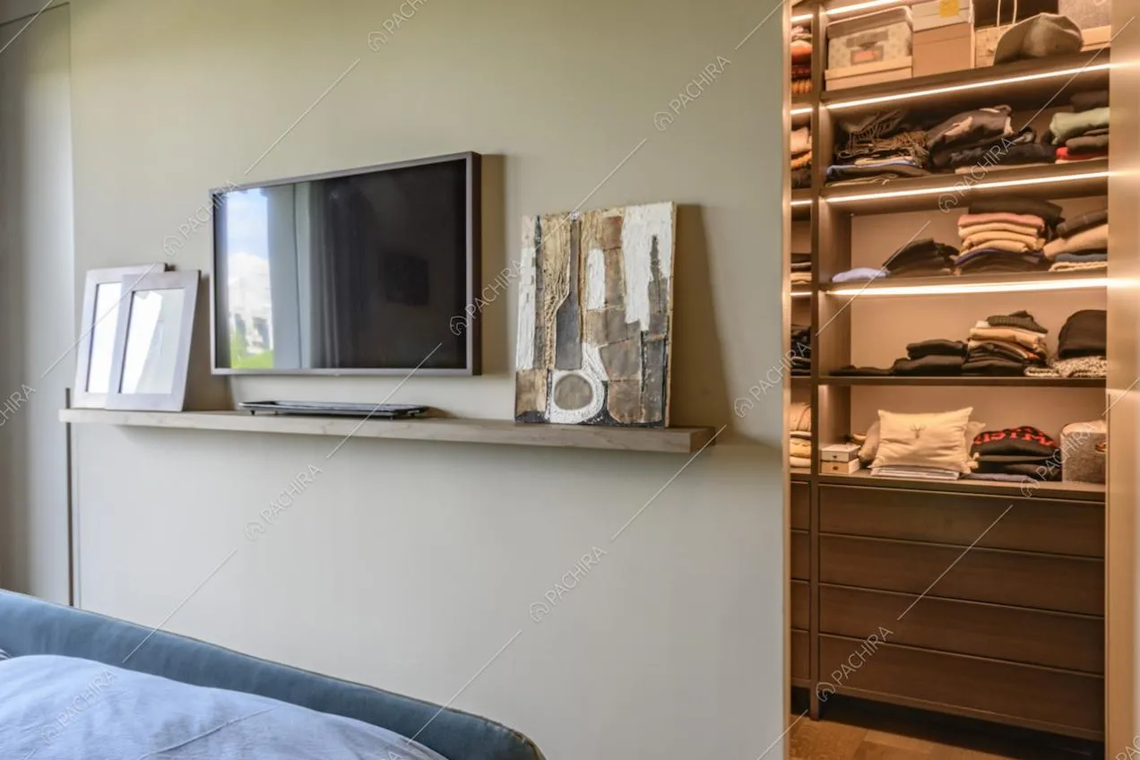 Televisore appeso alla parete e piccola mensola con portafoto