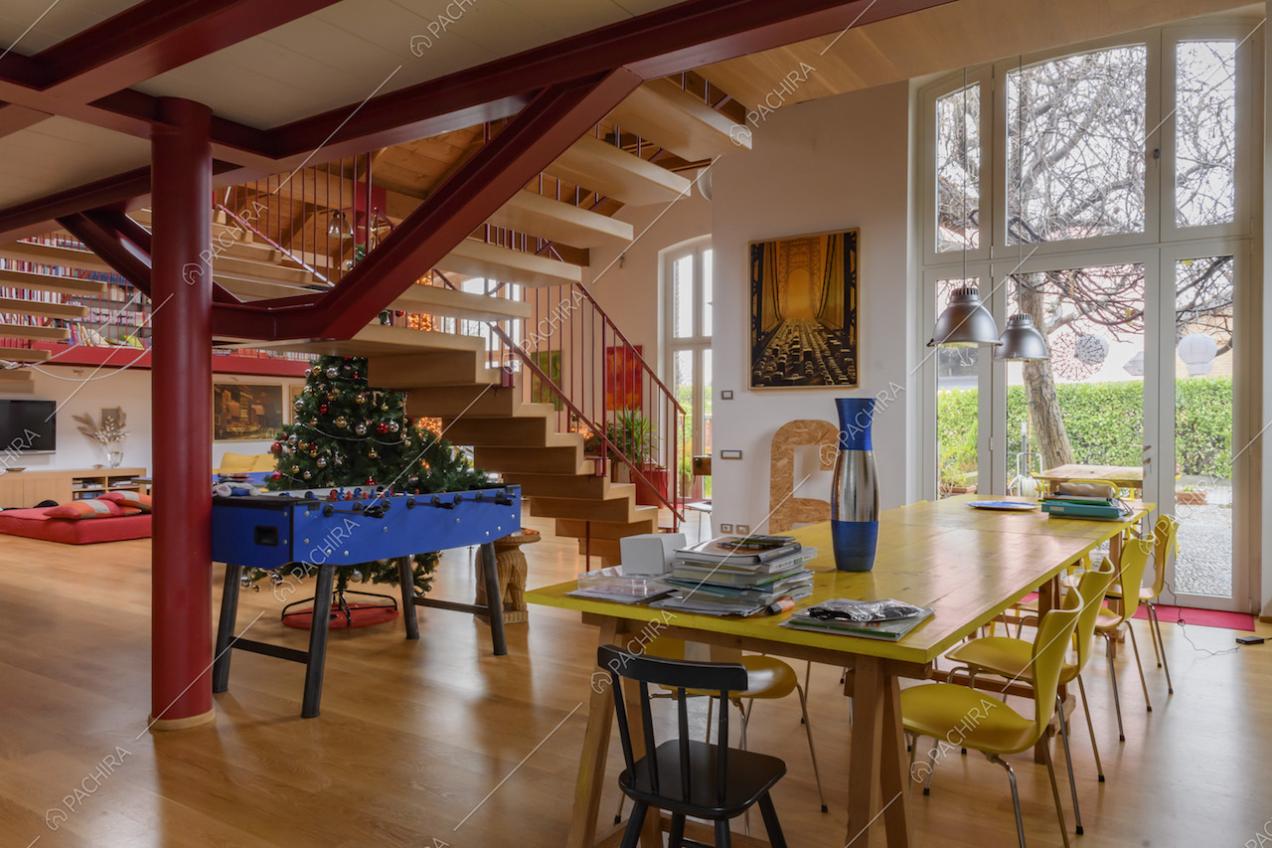 Salone con tavolo da pranzo giallo in legno, ampie vetrate e scale