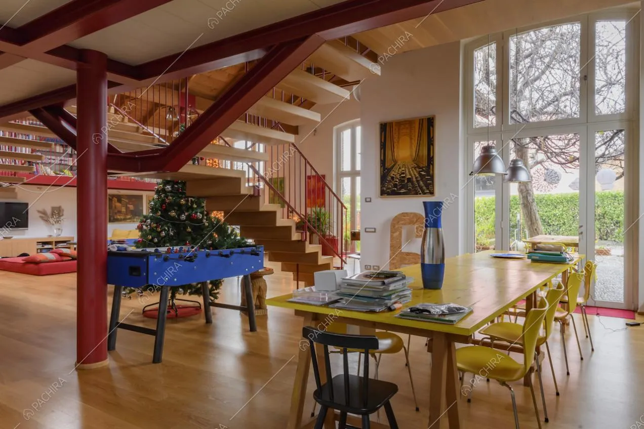 Salone con tavolo da pranzo giallo in legno, ampie vetrate e scale
