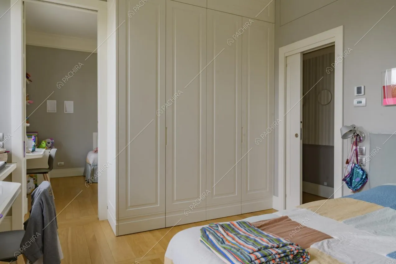 Camera da letto con pavimento in parquet, porta bianca scorrevole e vista su altra camera da letto