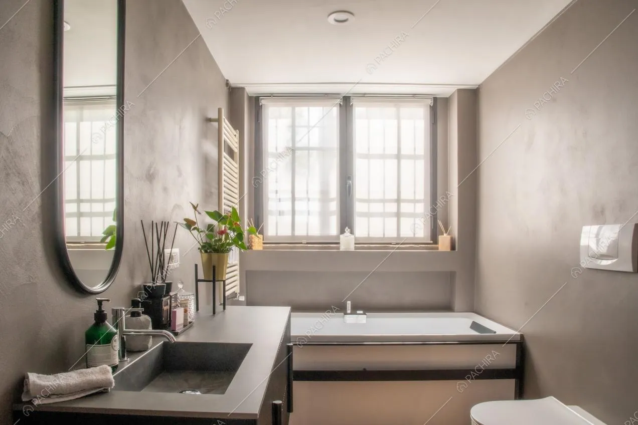 Bagno dalle pareti grigie ad effetto sabbia con specchio ovale e vasca da bagno
