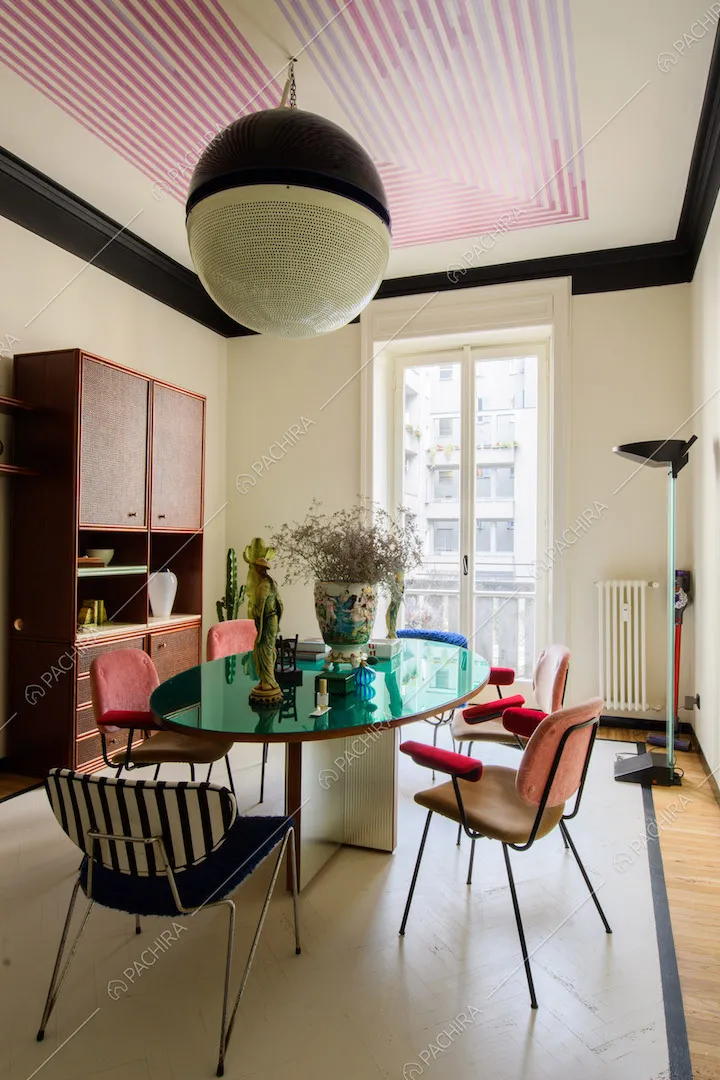 Sala da pranzo con tavolo ovale, sedie di design e soffitto con disegno geometrico fucsia