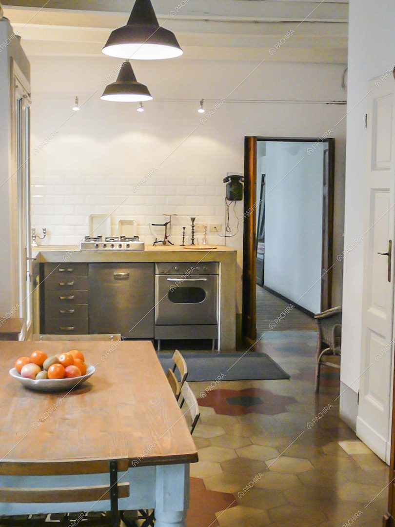 Cucina in acciaio a vista, pavimento in cementine e tavolo da pranzo in legno