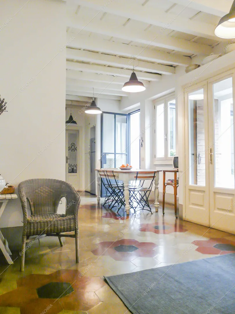 Sala con pavimento in cementine, porte-finestre bianche e soffitto bianco in travi in legno a vista