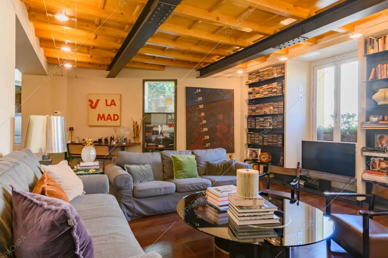 Salotto con divani grigi, librerie e soffitto in travi in legno a vista