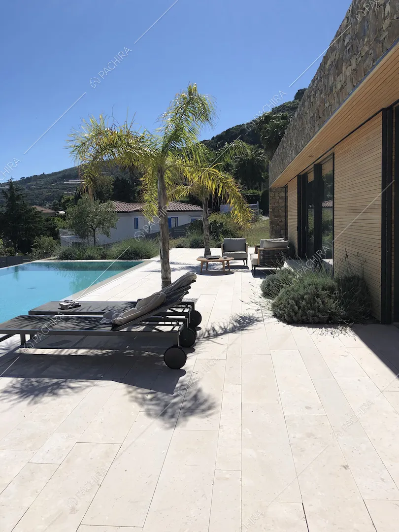 Terrazza con pavimentazione in lastre in pietra bianche, lettini neri, palme e piscina