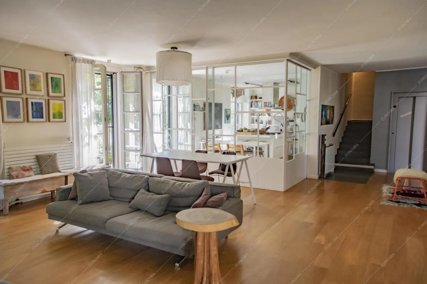 Salotto con pavimento in parquet e vista sulla cucina, separata da vetrate con infissi bianchi