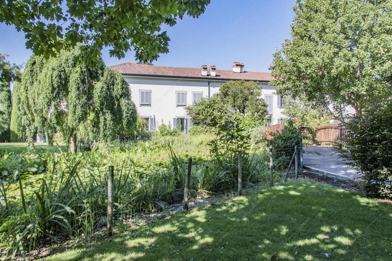 Dal giardino vista sul vialetto, sul piccolo ponte e sugli esterni bianchi della villa