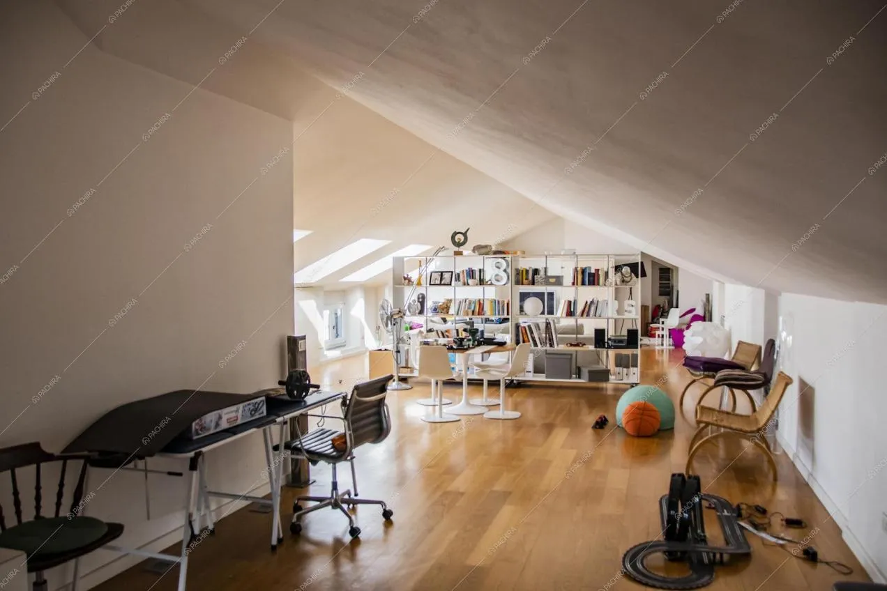 Mansarda dalle pareti e soffitto bianchi, pavimento in parquet e libreria che separa gli ambienti