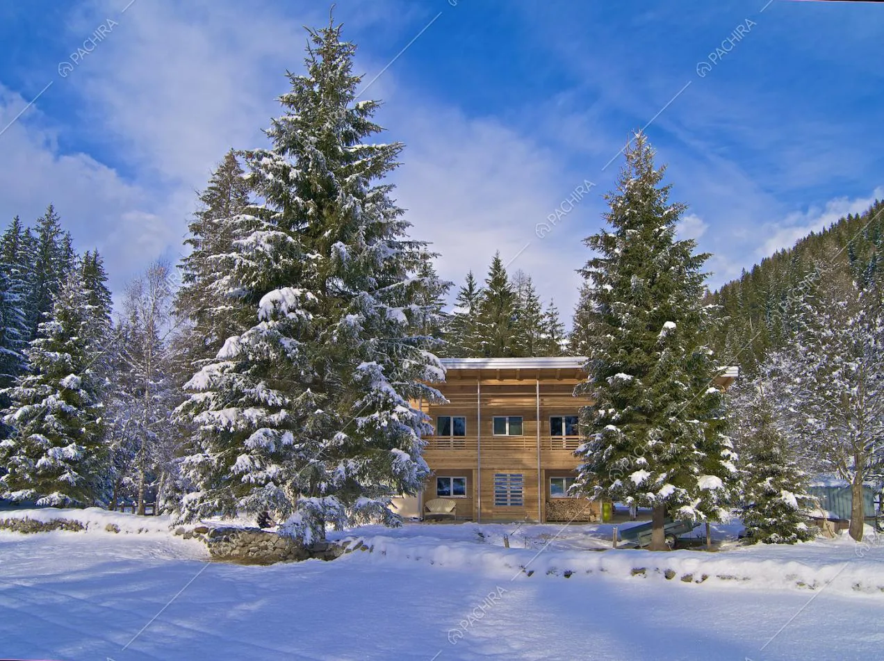 Vista sullo chalet a due piani dagli esterni innevati e con grandi alberi sempreverdi