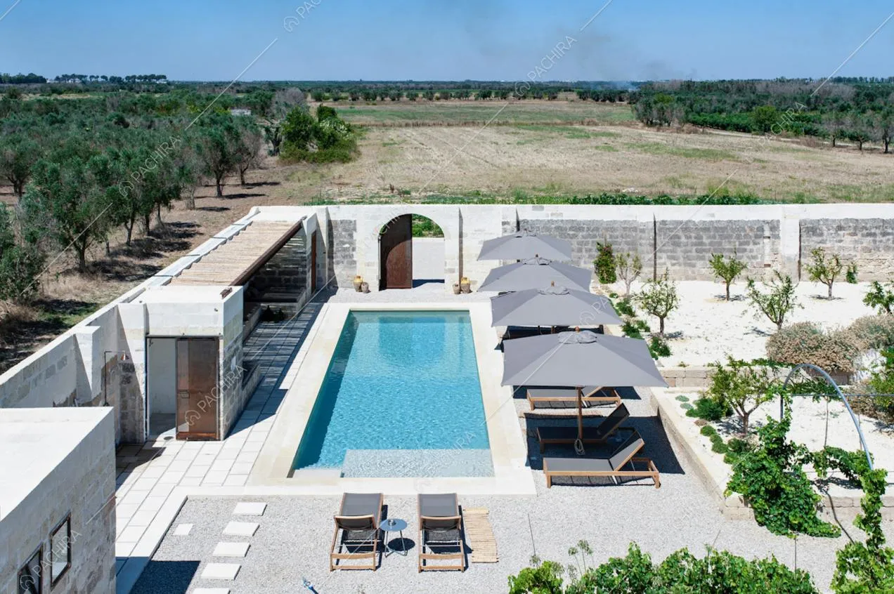 Ampio patio con piscina, ombrelloni e piante, circondato da muri in pietra