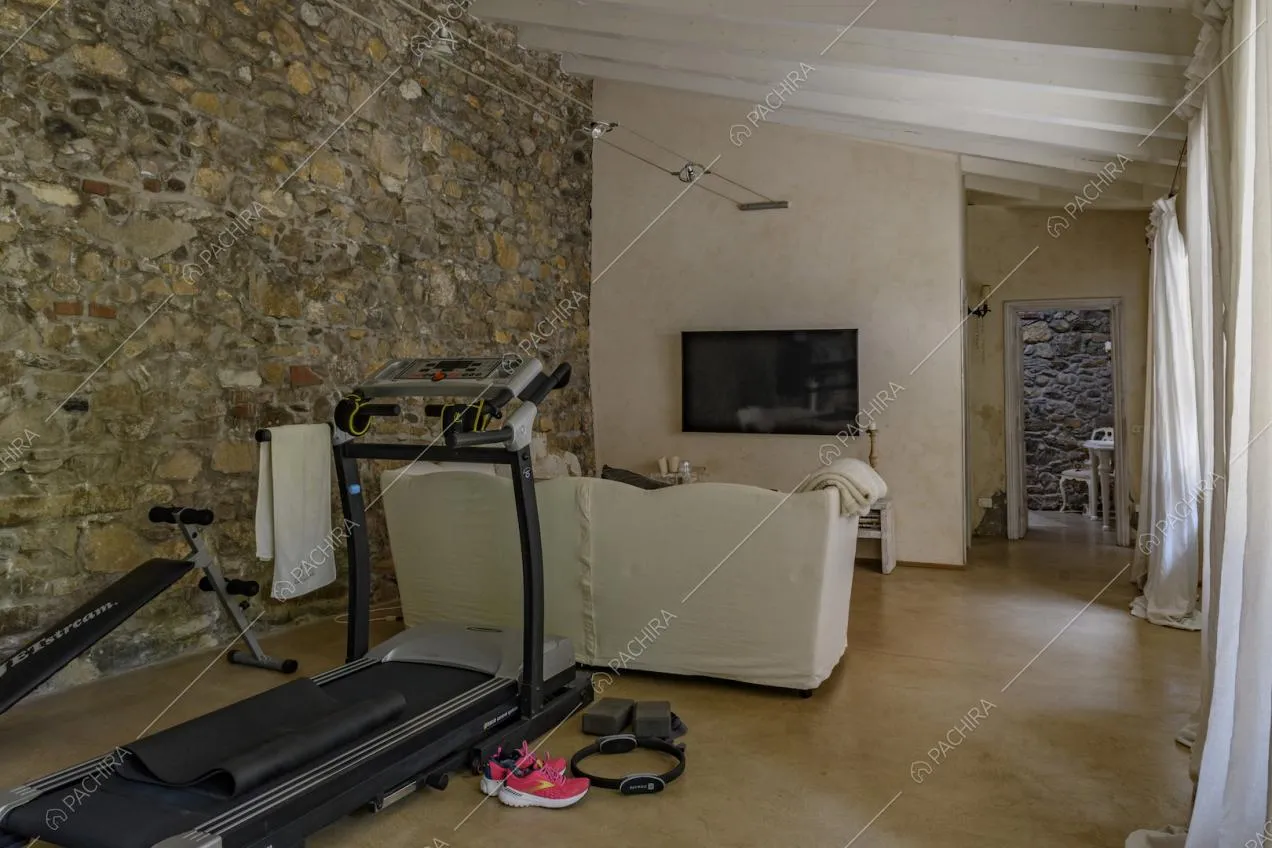Salotto con pavimento in cemento lisciato, parete in pietra e soffitto con travi in legno bianco a vista