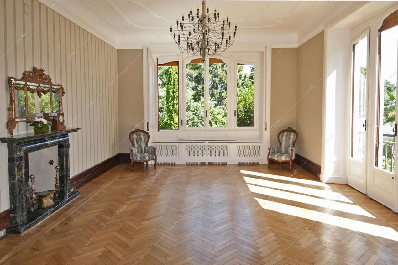 Salone con camino, ampie vetrate, pavimento in parquet a spina di pesce e pareti beige