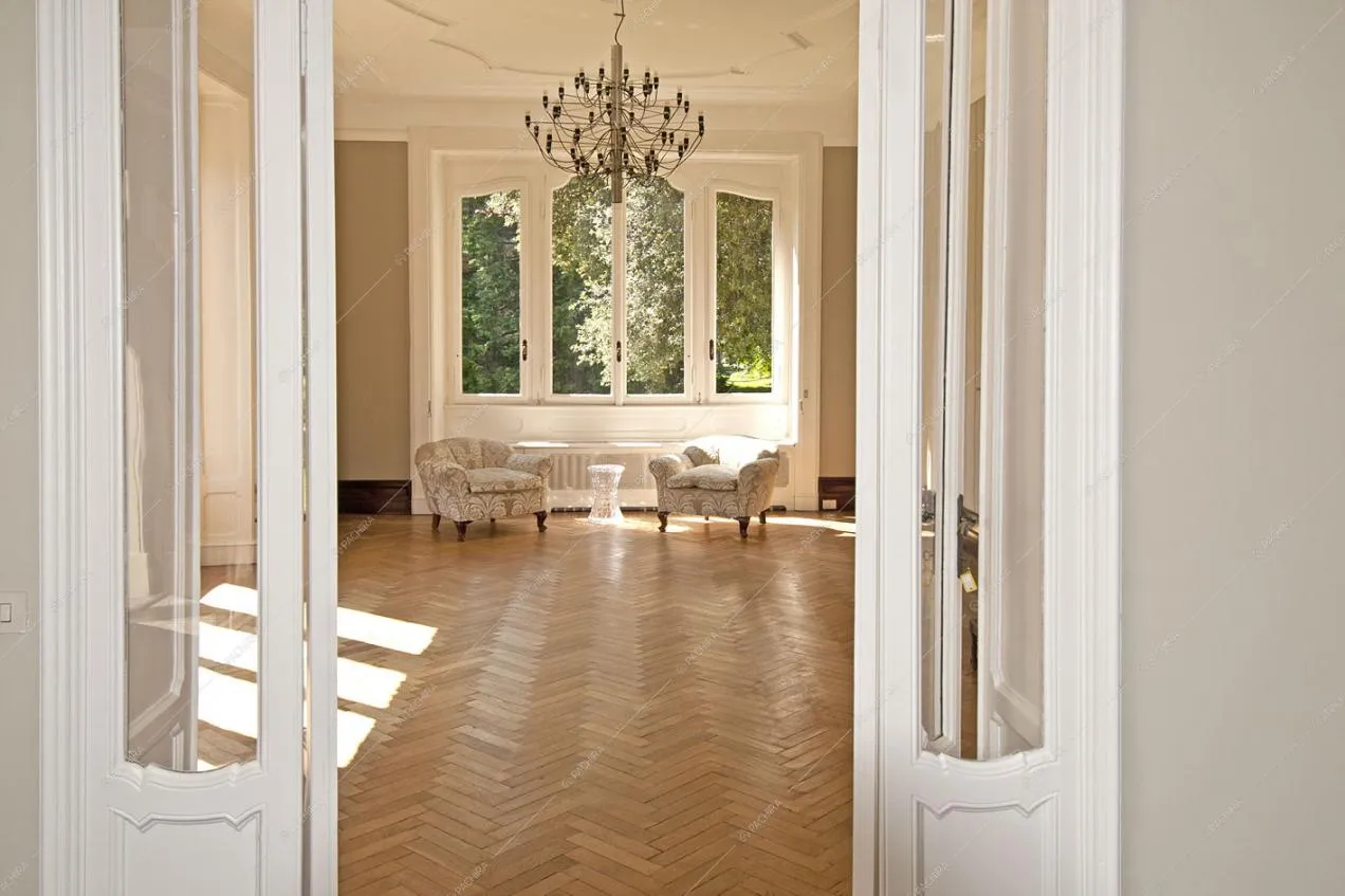 Dalla porta accesso al luminoso salone con pavimento in parquet a spina di pesce, poltrone classiche e lampadario antico