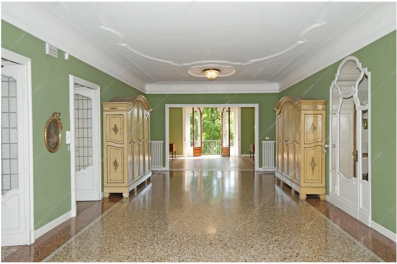 Corridoio dalle pareti verdi, soffitto con boiserie e vista sul balcone con porta-finestra