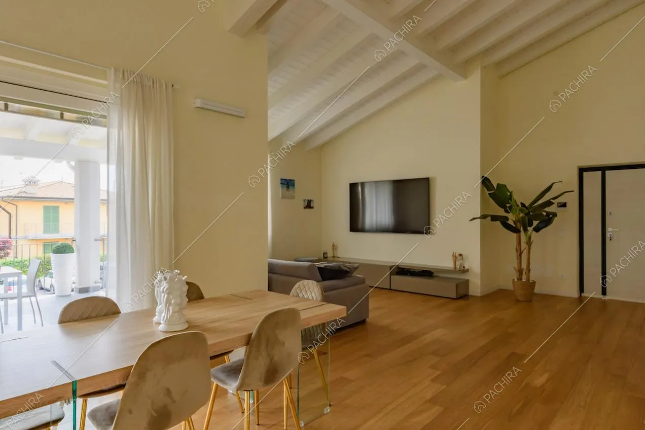 Travi bianche a vista sul soffitto, tavolo da pranzo e pavimento in parquet nella zona living