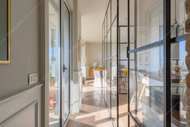 Corridoio con parete grigia e boiserie, pavimento in parquet e parete vetrata industriale