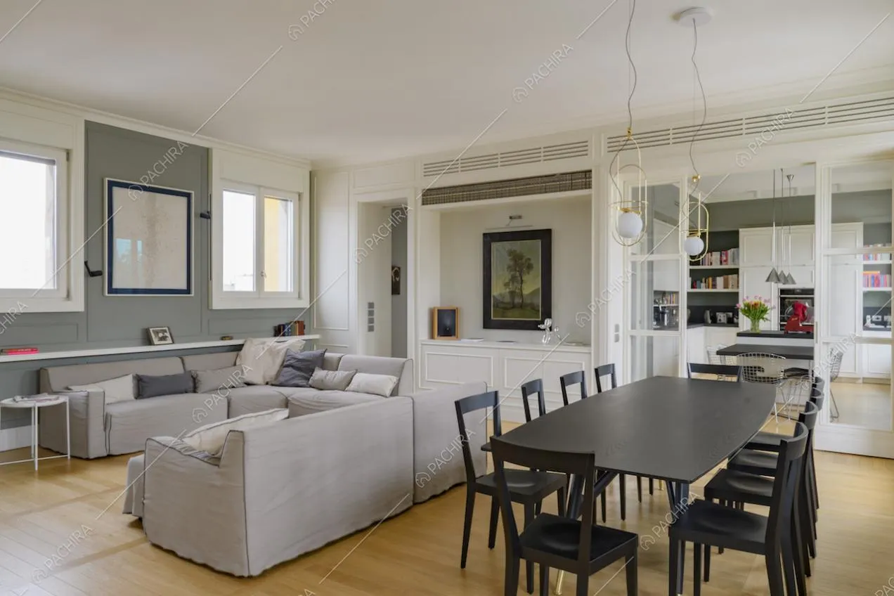 Sala con divani grigi, tavolo nero e cucina separata da porte a vetri