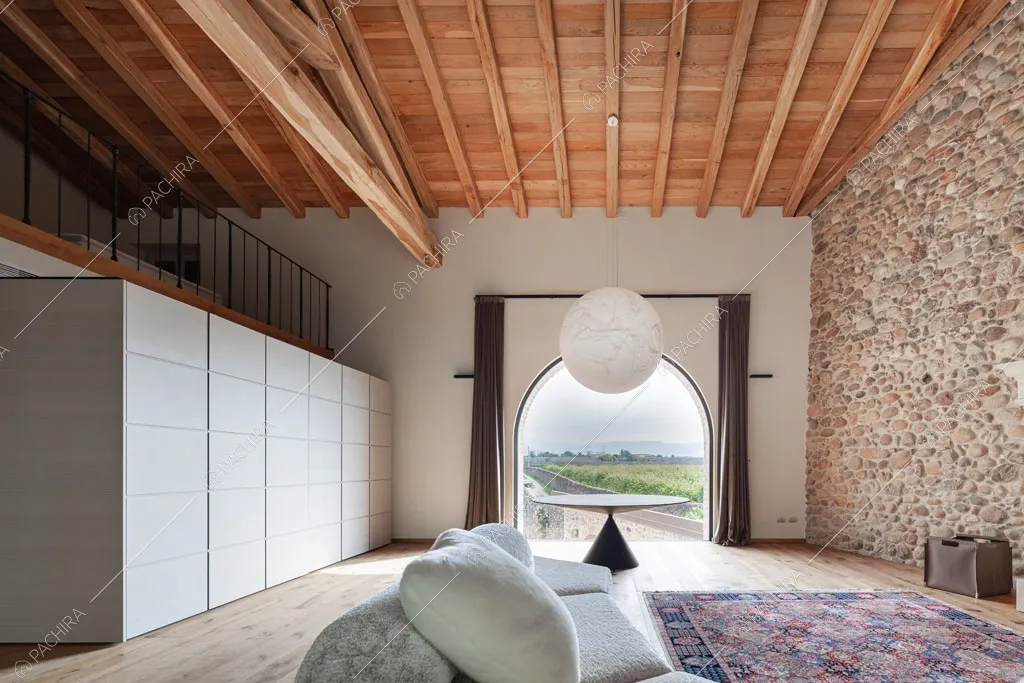 Sala con parete in pietra a vista e soppalco nella villa Ghibli, location in stile contemporaneo a Verona