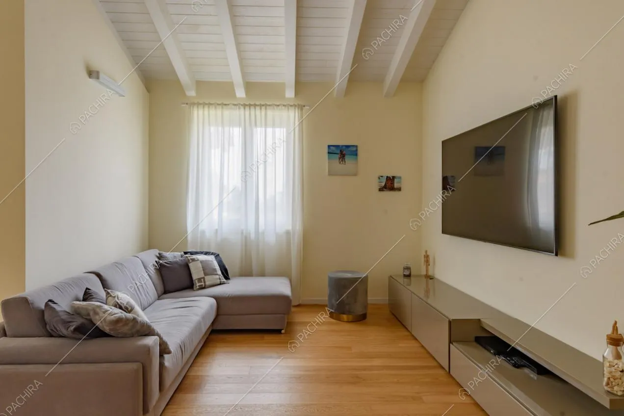 Pareti gialle, pavimento in parquet e travi bianche a vista sul soffitto della sala