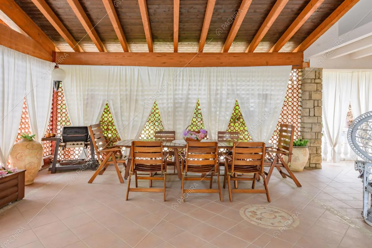 Tavolo da pranzo e sedie in legno nella luminosa veranda con travi a vista