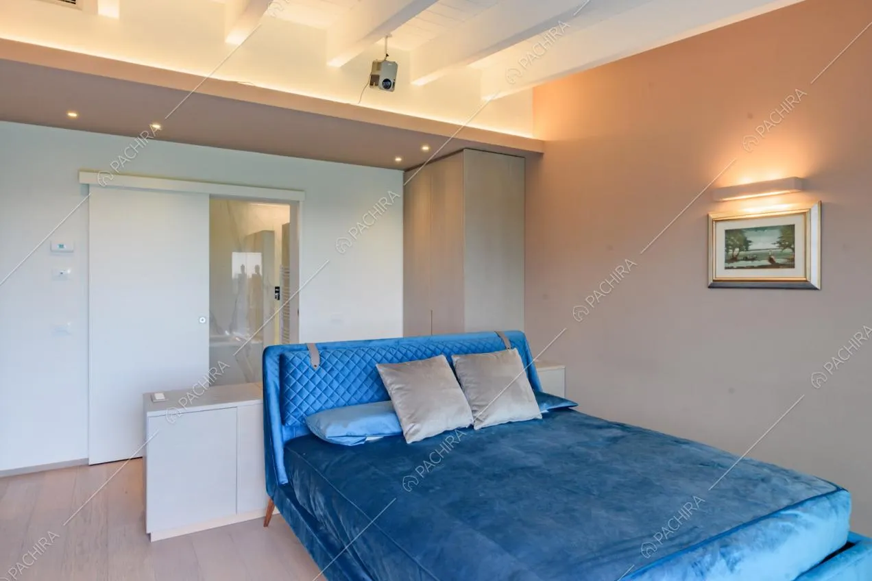 Letto matrimoniale blu nella camera con pavimento in parquet e travi a vista sul soffitto