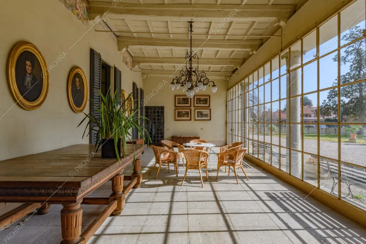 Veranda con soffitto in travi in legno e vista sul grande giardino tramite le vetrate