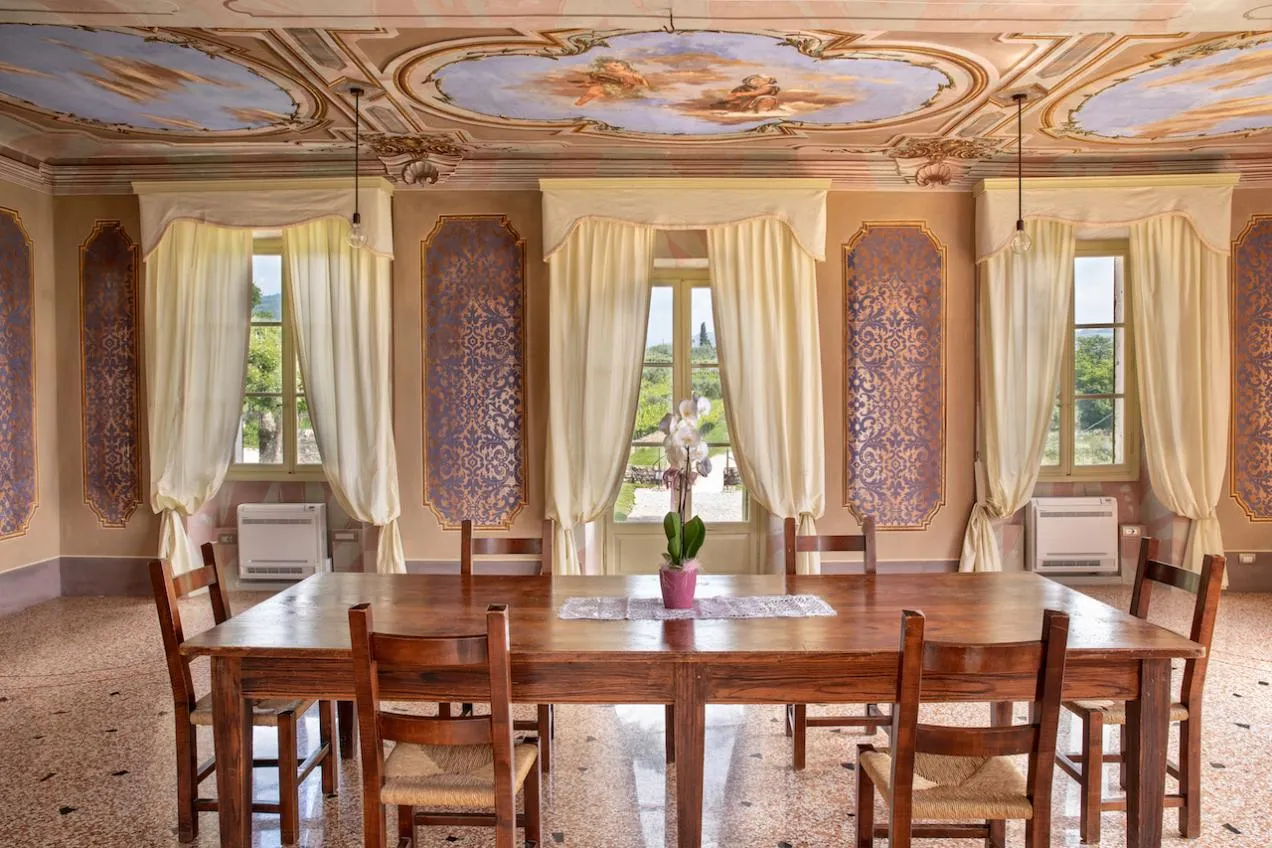 Luminoso salone con vista sui colli veneti con tavolo da pranzo in legno, tende bianche e soffitto affrescato
