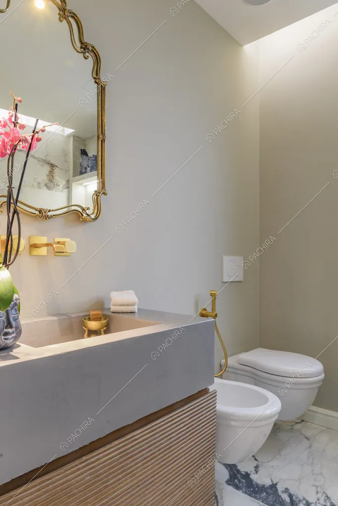 Bagno dal pavimento in marmo con specchio dalla cornice dorata, così come la rubinetteria