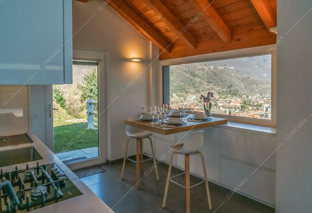 Nella cucina bianca con fornelli a gas, vista sul lago dal bancone in legno e sgabelli