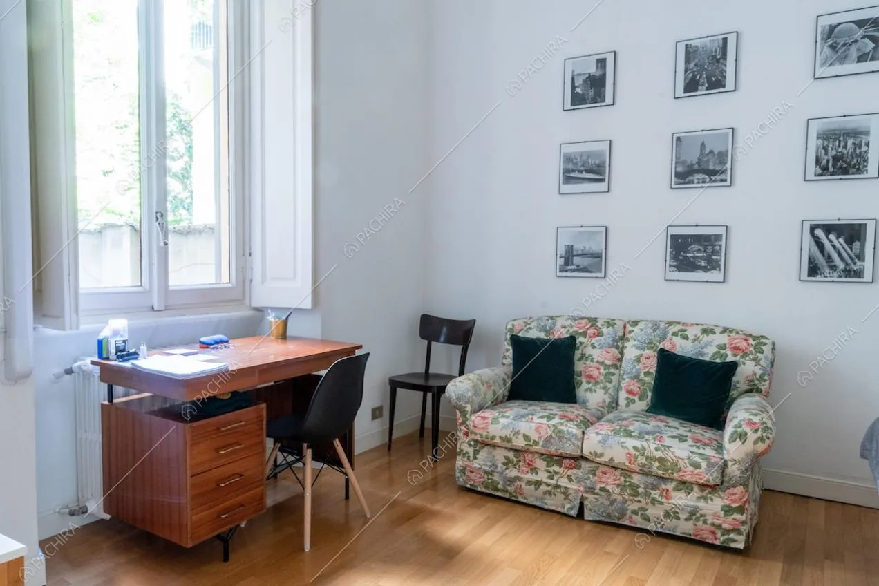 Scrivania e divano nella luminosa camera con alti soffitti, pavimento in parquet e pareti bianche